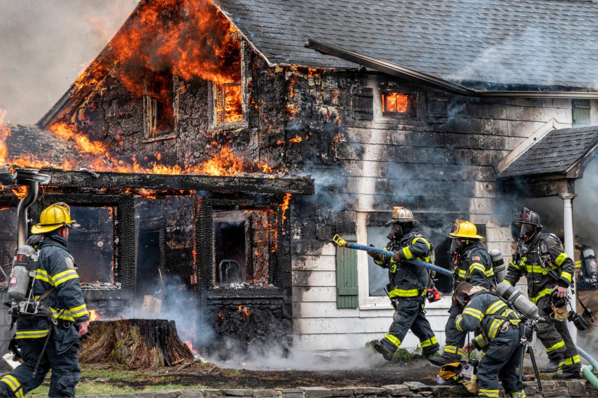 A group of firefighters are fighting a fire in front of a house during a fire safety inspection.
